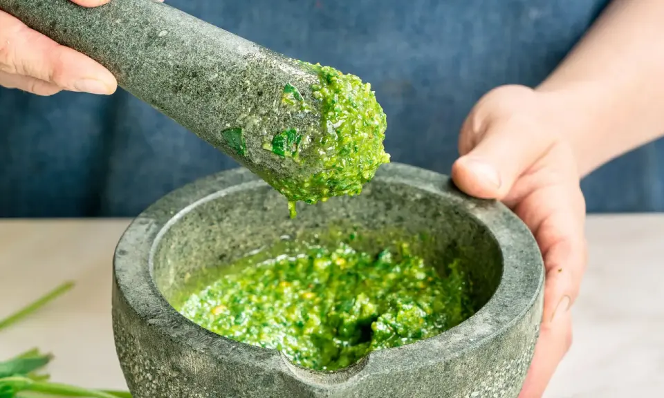 Frische Kräuter werden im Mörser zu einem leuchtend grünen pesto genovese zermahlen.