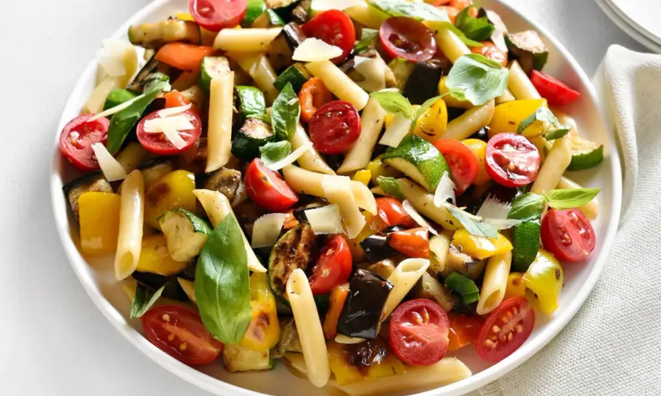 Bunter Nudelsalat ohne Mayo mit Penne, gegrilltem Gemüse wie Zucchini, Aubergine, Paprika und Kirschtomaten, garniert mit Basilikum und Parmesan.