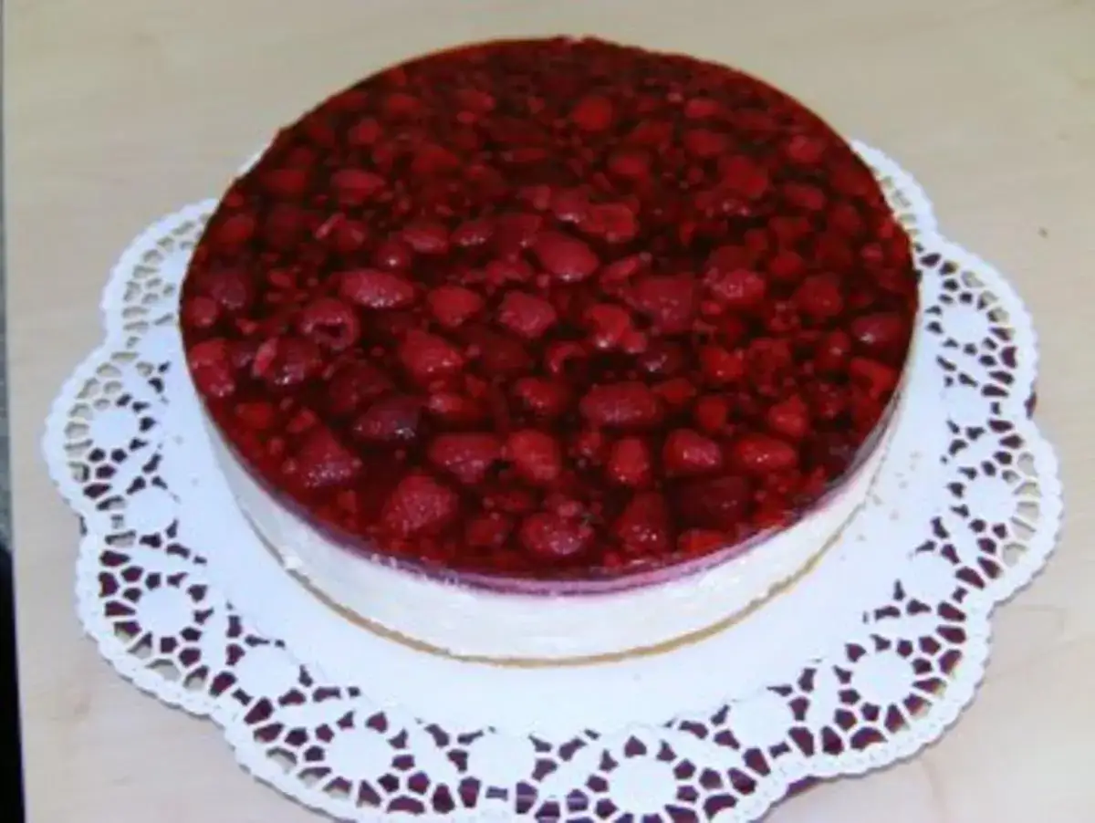 Himbeer Joghurt Torte mit frischen Beeren und cremigem Boden, serviert auf einer zarten Tortenspitze.
