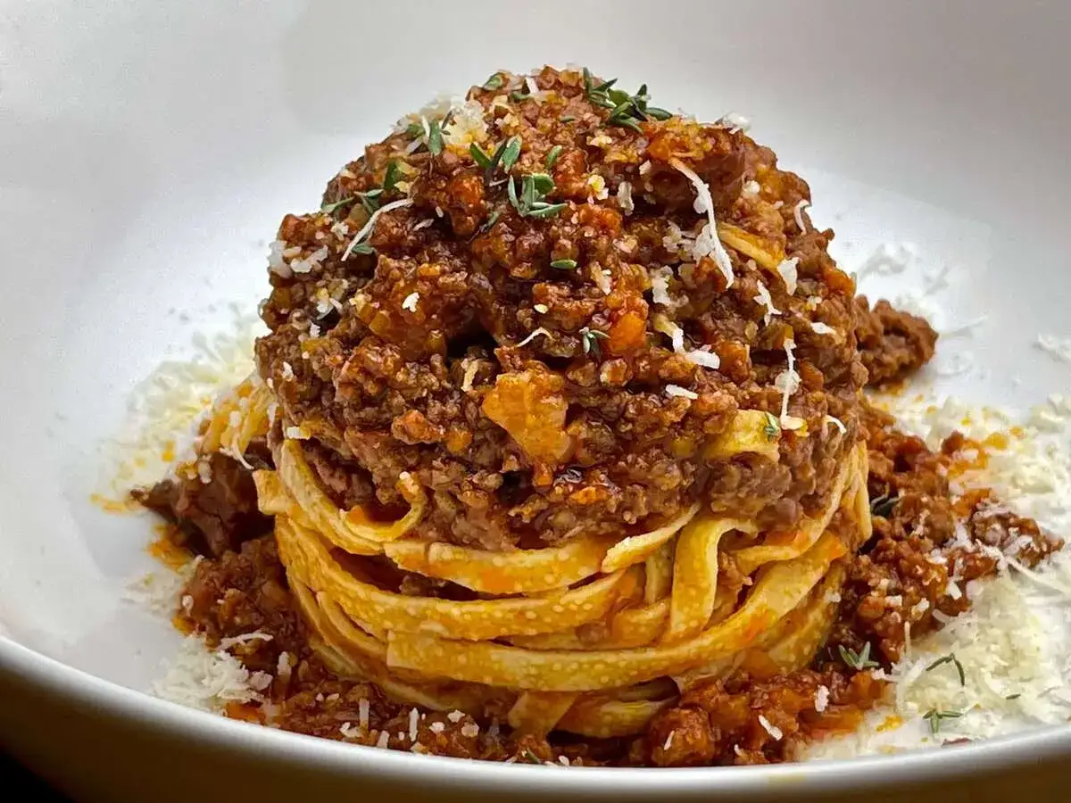 Ein Turm aus Tagliatelle, bedeckt mit einer reichhaltigen, klassischen Bolognese-Sauce und bestreut mit Parmesan und Kr&auml;utern.