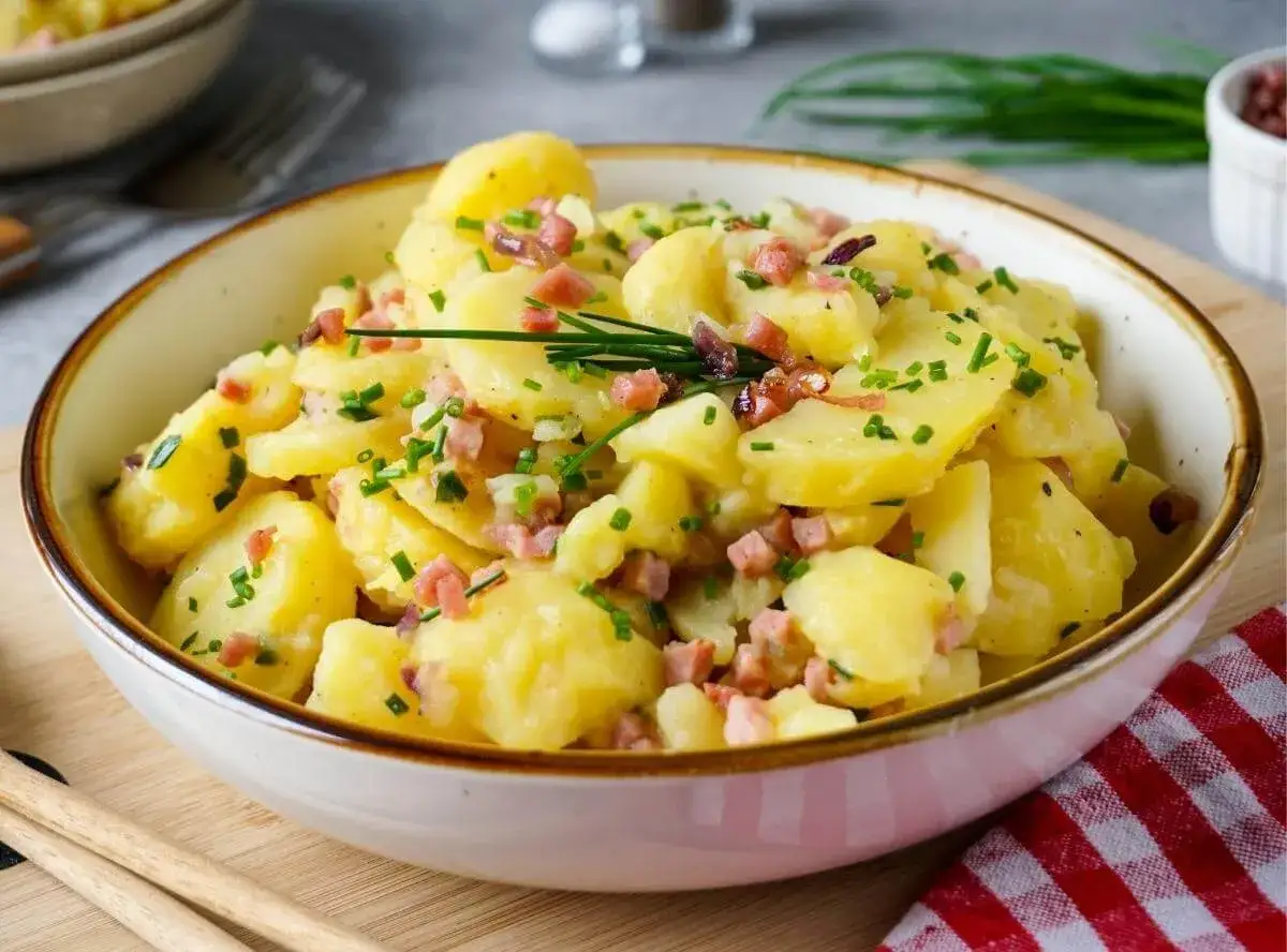Schüssel mit warmem Kartoffelsalat, garniert mit Speckwürfeln und Schnittlauch. Ein Klassiker, der immer schmeckt.