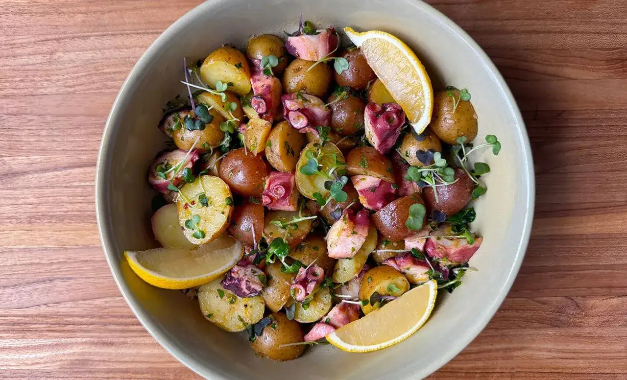 Ein köstlicher Pulpo Salat Original mit kleinen Kartoffeln, zarten Tintenfischstücken, frischen Kräutern und Zitronenspalten.