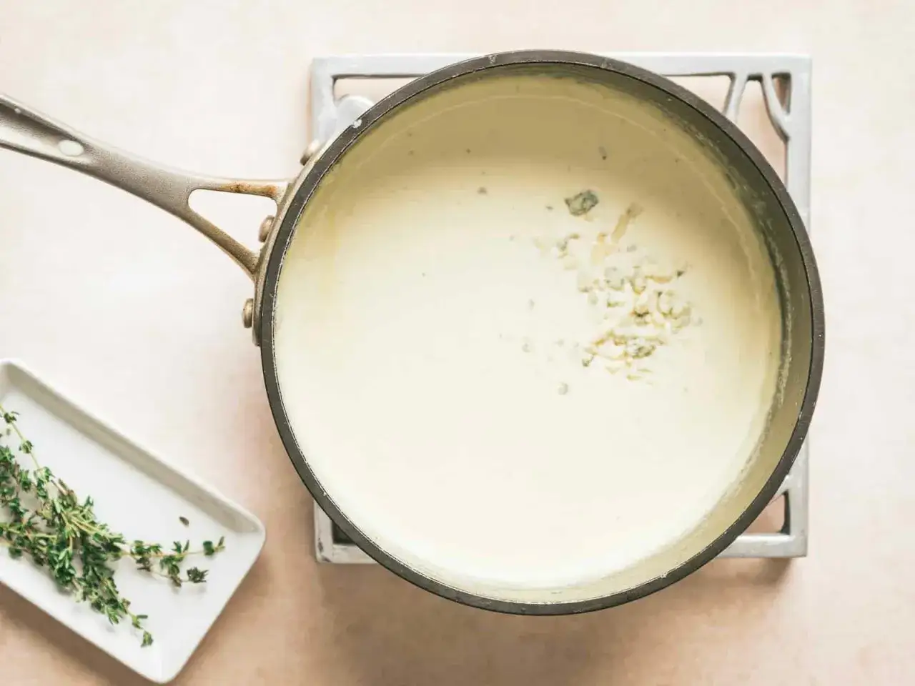 Cremige Gorgonzola-Sauce schmilzt in einem Topf, daneben ein Zweig Thymian.
