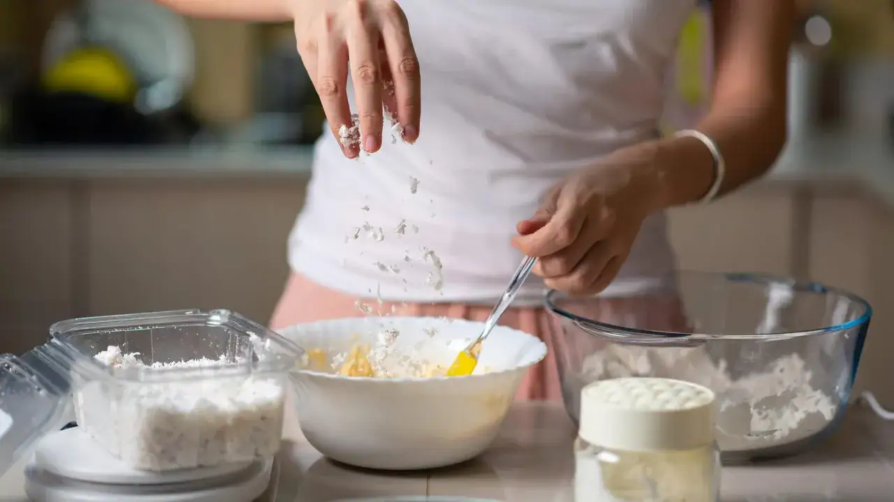 Hände streuen Haferflocken in eine Schüssel, um gesunde Kekse zu backen.