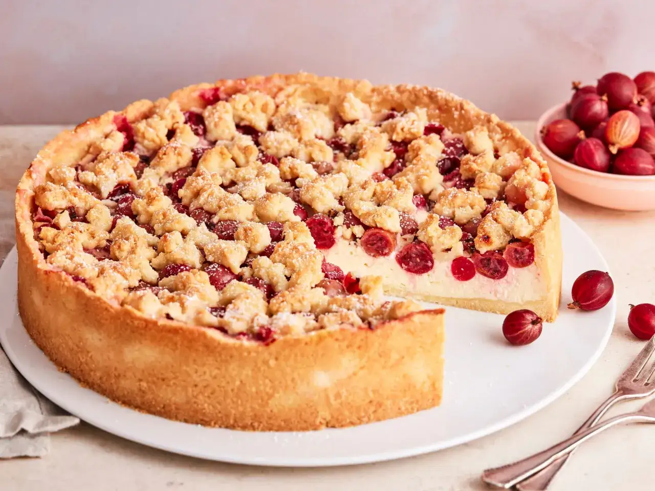 Ein saftiger Stachelbeerkuchen mit knusprigen Streuseln, verlockend auf einem wei&szlig;en Teller pr&auml;sentiert. Daneben eine Schale voller frischer Stachelbeeren.