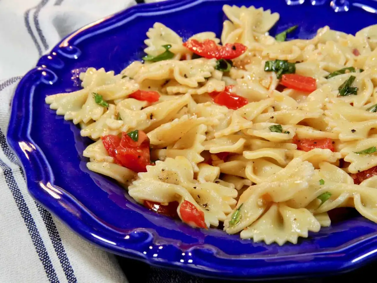Farfalle-Nudeln mit frischen Tomaten und Basilikum, serviert auf einem blauen Teller. Ein Hauch von italienischer Tomatensauce macht dieses Gericht unwiderstehlich.