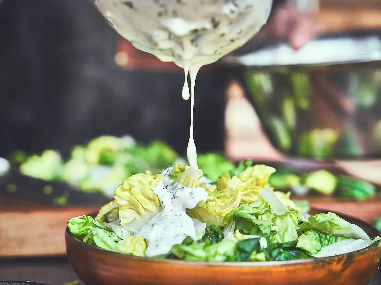 Cremiger ranch dressing fließt auf einen frischen Salat in einer Holzschüssel.