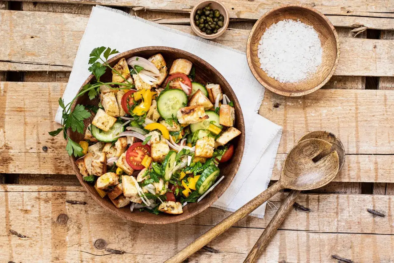 Ein bunter Panzanella Salat mit ger&ouml;stetem Brot, Tomaten, Gurken, Paprika und Zwiebeln in einer Holzschale.