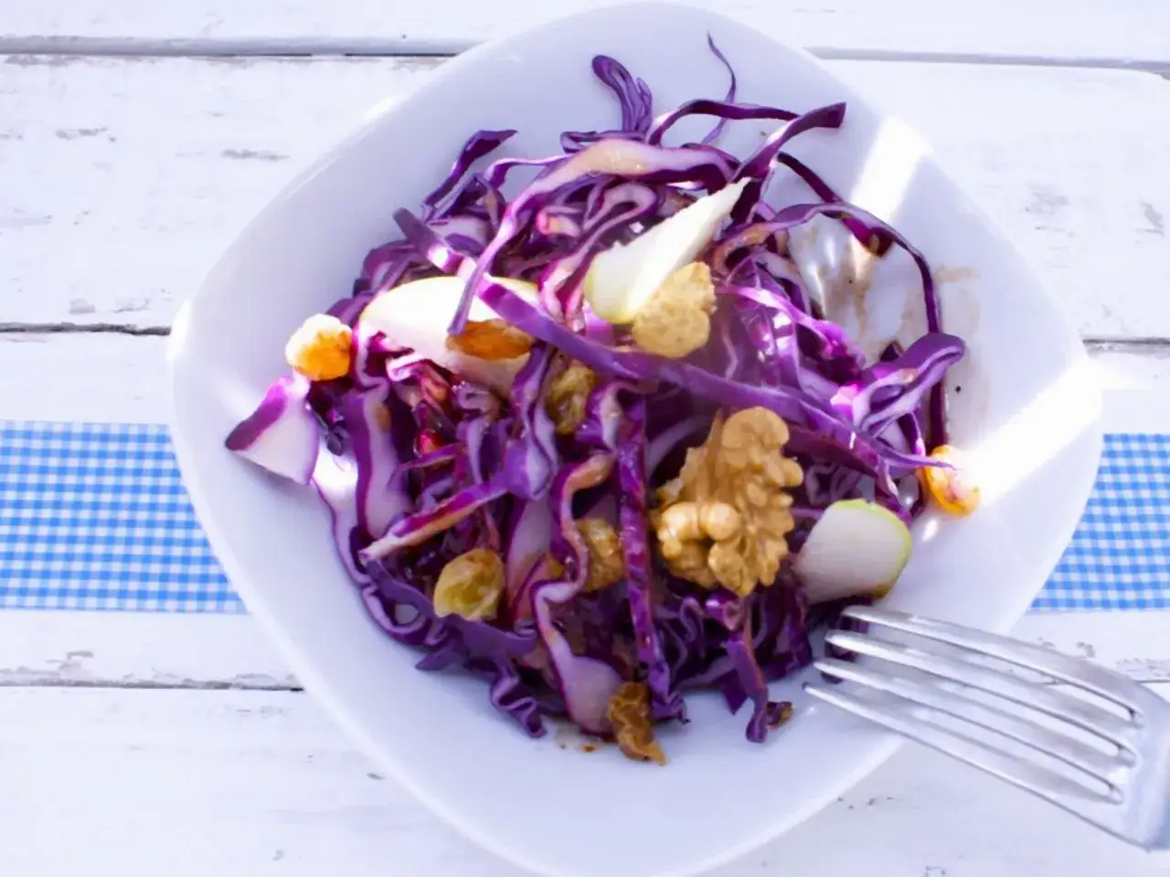 Ein bunter rotkohl salat mit Äpfeln, Rosinen und Walnüssen auf einem weißen Teller.