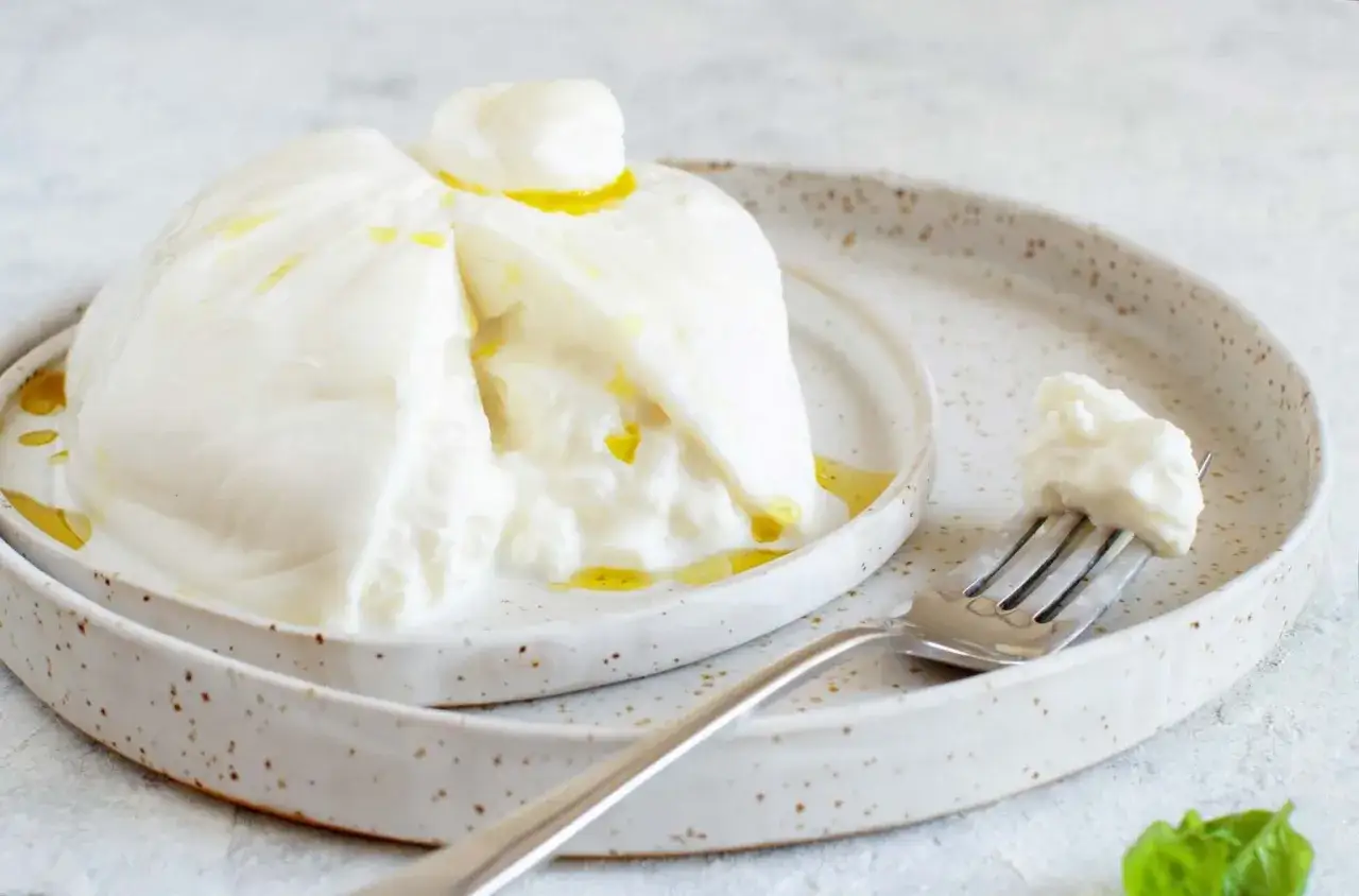 Ein cremiger Burrata-K&auml;se auf einem Teller, betr&auml;ufelt mit Oliven&ouml;l. Was ist Burrata? Ein frischer Mozzarella-Beutel mit cremigem Kern.