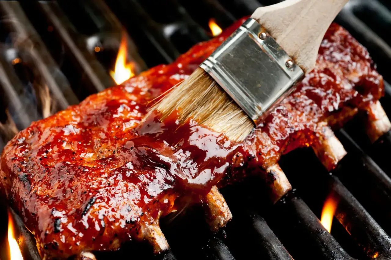 Spareribs werden mit einer köstlichen Spareribs Marinade auf dem Grill glasiert, während Flammen aufsteigen.