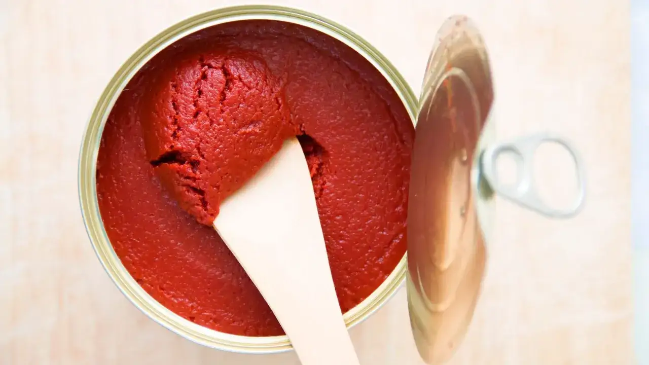 Ein offener Beh&auml;lter mit leuchtend rotem Tomatenmark, das mit einem Holzspatel entnommen wird. Perfekt als Tomatenmark-Ersatz f&uuml;r Saucen und Eint&ouml;pfe.