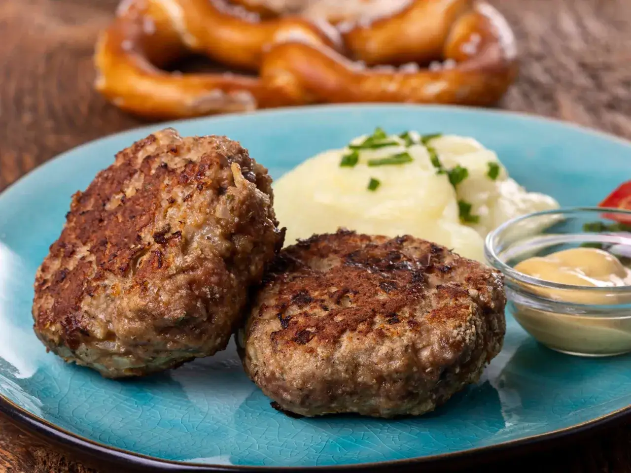 Zwei goldbraune Frikadellen mit Kartoffelpüree und Senf. Ein Brezel im Hintergrund. Ein tolles Frikadellen Rezept für jeden Anlass.