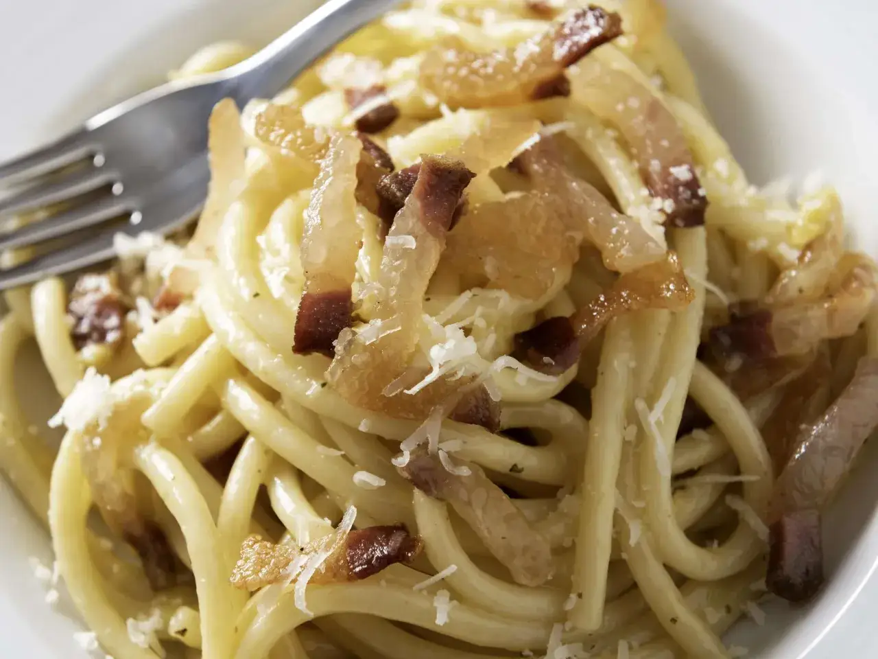 Ein Teller cremiger Carbonara-Pasta mit knusprigem Guanciale und frisch geriebenem Parmesan. Ein Gabel liegt bereit.