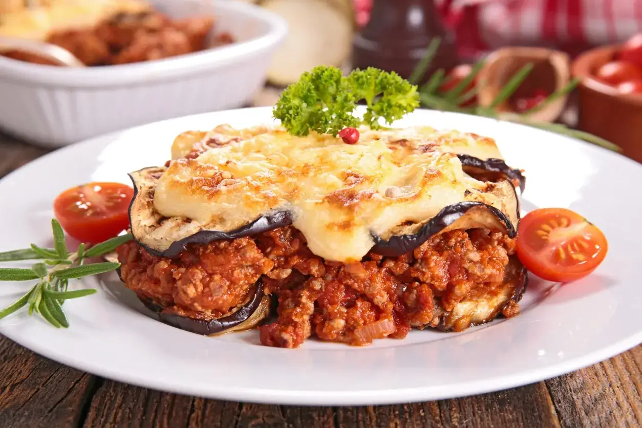 Moussaka, ein Klassiker der griechischen Rezepte, mit geschichteten Auberginen, Hackfleisch und cremiger Béchamelsauce, garniert mit Petersilie und Tomaten.