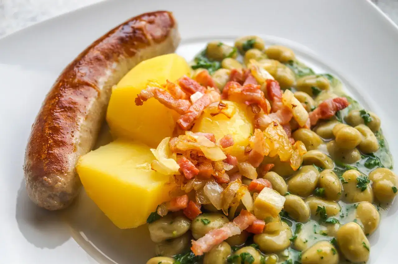 Deftiges Gericht mit Bratwurst, Kartoffeln und dicken Bohnen in cremiger Sauce, garniert mit Speck und Zwiebeln. Ein klassisches dicke bohnen rezept.