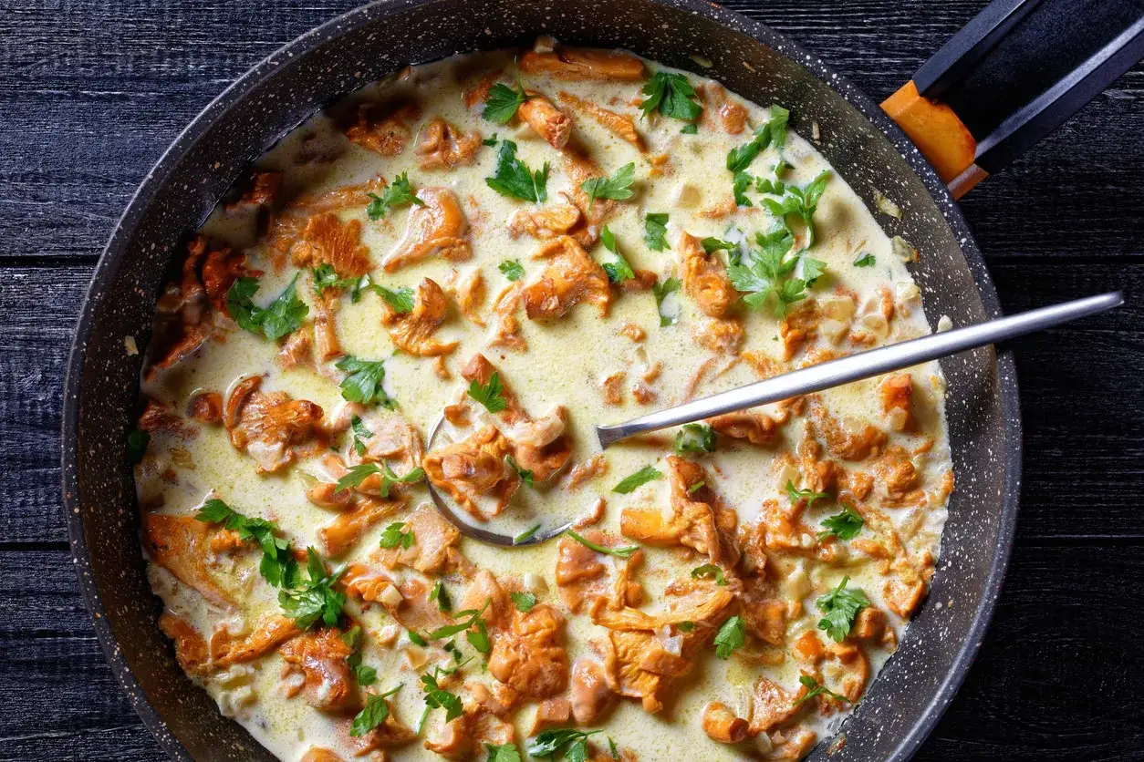 Pfifferlinge in cremiger Rahmsauce, garniert mit Petersilie, in einer Pfanne. Ein L&ouml;ffel ragt aus der k&ouml;stlichen Speise.