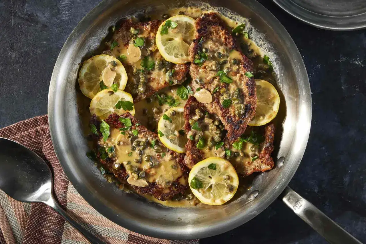 Piccata in einer Pfanne mit Zitronenscheiben, Kapern und Petersilie. Ein k&ouml;stliches Gericht, das man probieren muss!