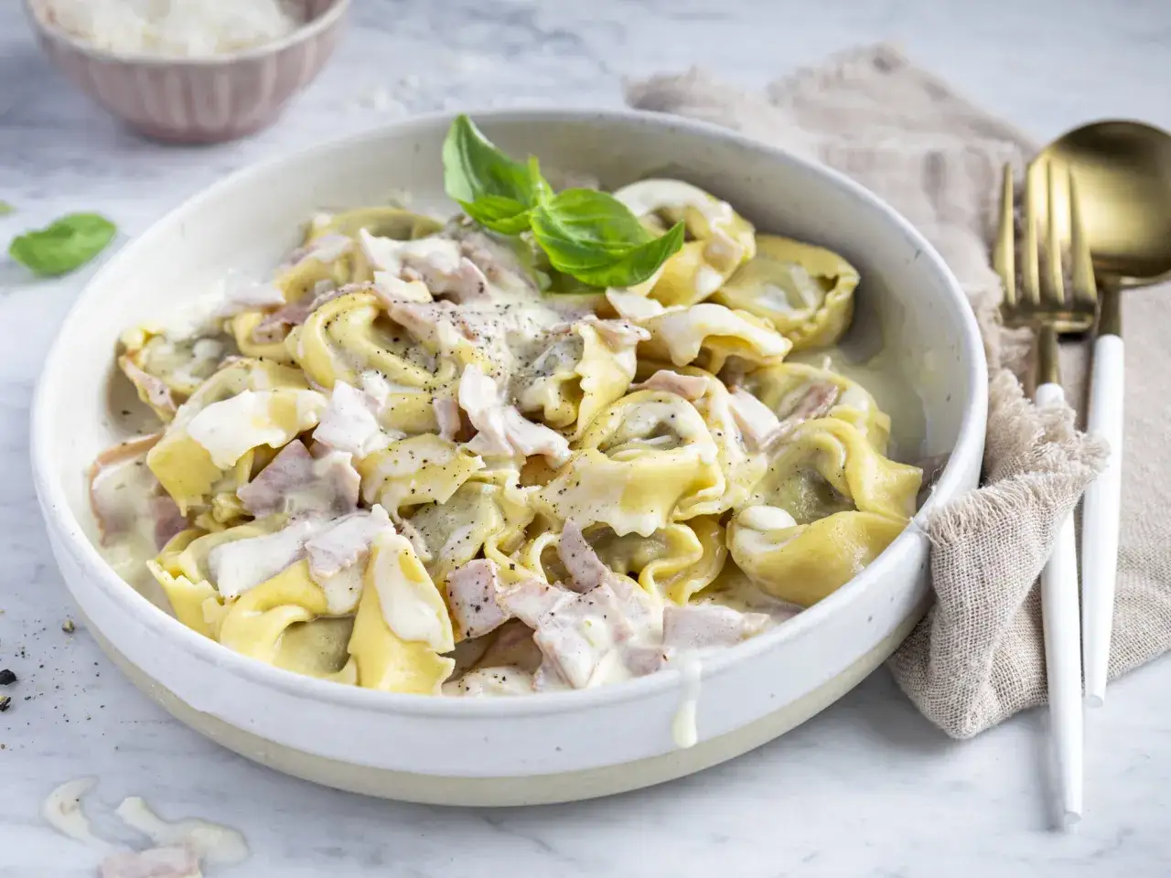 Ein Teller mit cremigen Tortellini alla Panna, garniert mit Basilikum und bestreut mit schwarzem Pfeffer.