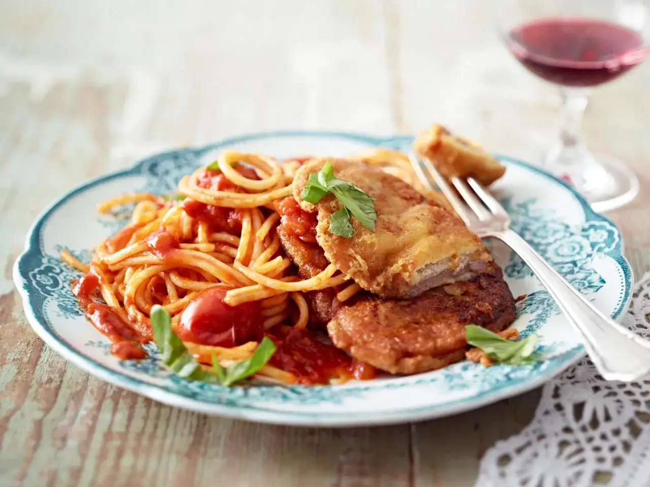 Piccata Milanese: goldbraune Schnitzel auf Spaghetti mit Tomatensauce und frischem Basilikum, dazu ein Glas Rotwein.