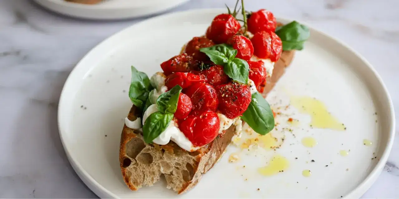 Ger&ouml;stetes Brot mit cremigem K&auml;se, Kirschtomaten und Basilikum, verfeinert mit einem Hauch von Pesto Rosso.