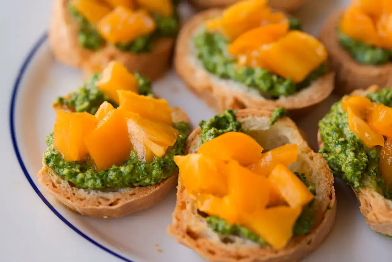 Knusprige Bruschetta-Scheiben mit leuchtend gr&uuml;nem Rucola Pesto und saftigen, orangefarbenen Tomatenw&uuml;rfeln.