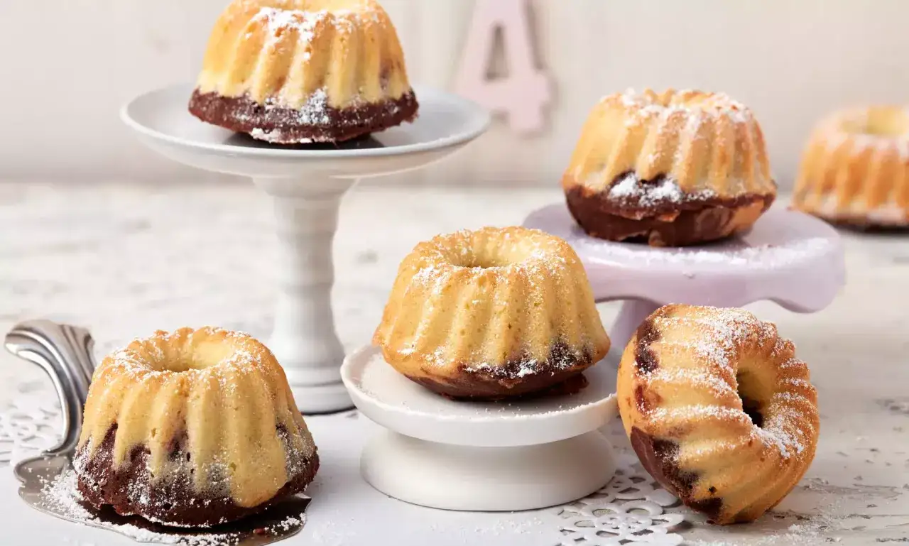 Mehrere mini Gugelhupf mit Puderzucker best&auml;ubt, auf verschiedenen Etageren arrangiert.