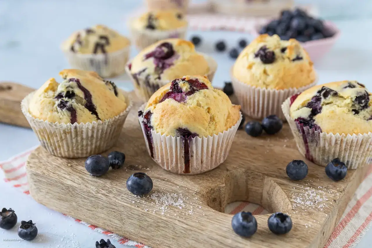 Saftige blaubeer muffins mit frischen Beeren, auf einem Holzbrett arrangiert. Ein Genuss f&uuml;r Augen und Gaumen!