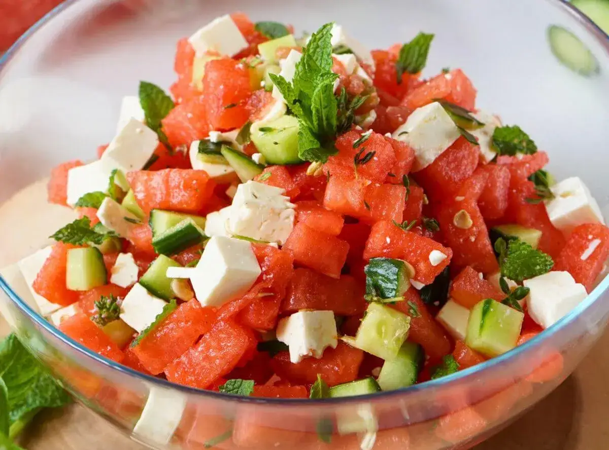 Erfrischender Feta Melonen Salat mit Gurkenstücken und Minze in einer Glasschüssel.