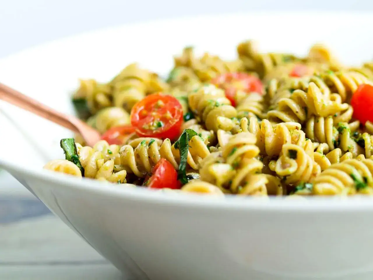 Bester Spaghettisalat mit Pesto, Kirschtomaten und frischem Basilikum in einer weißen Schüssel.