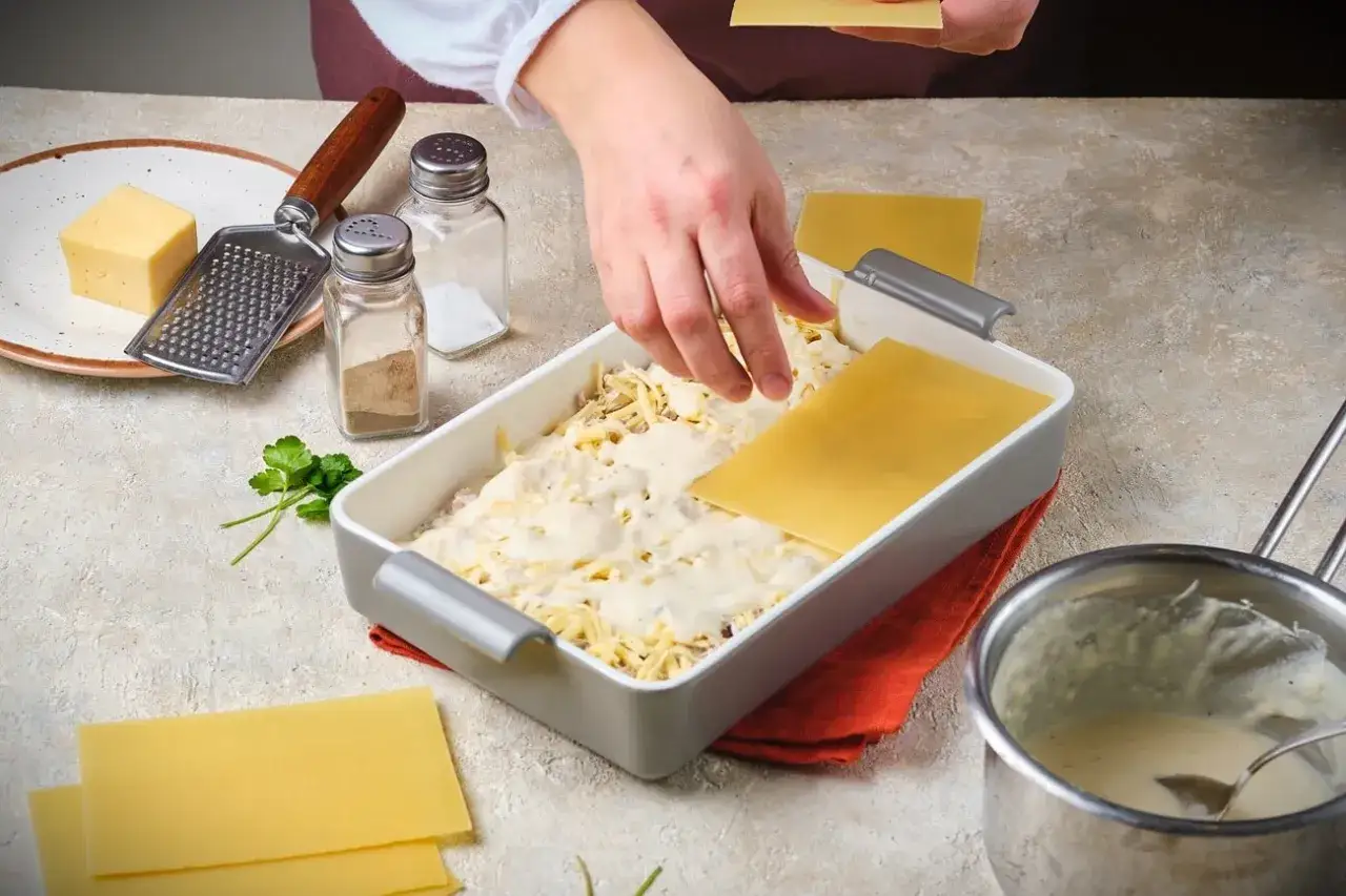 H&auml;nde legen Lasagneplatten f&uuml;r ein authentisches italienisches Lasagne Rezept. K&auml;se, Gew&uuml;rze und ein Kochtopf sind bereit.