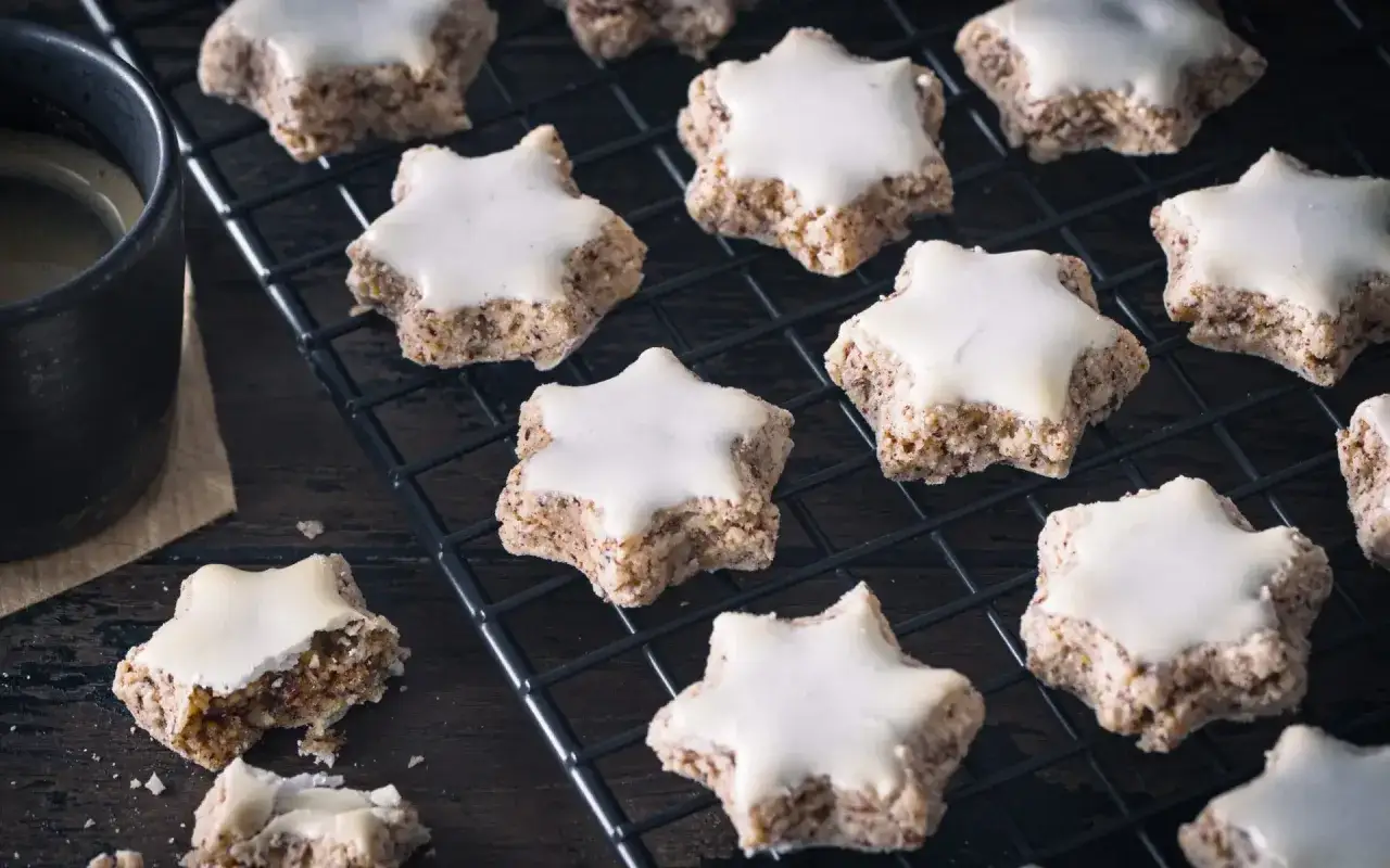 Zimtsterne rezept klassisch: Sterne aus N&uuml;ssen, mit Zuckerguss, auf einem Gitter, daneben eine Tasse Kaffee.