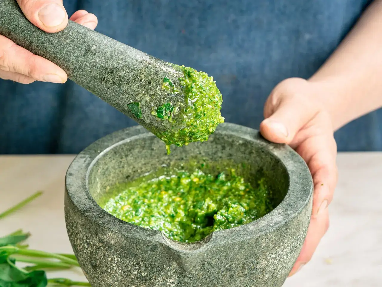 Frische Kr&auml;uter werden im M&ouml;rser zu einem leuchtend gr&uuml;nen Pesto Genovese zermahlen.