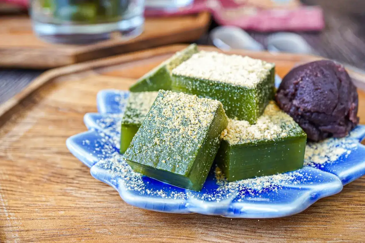 Grüne, würfelige Süßigkeiten, die an was ist Gelatine erinnern, bestreut mit hellem Pulver, serviert auf einer blauen Schale mit einer Kugel dunkler Paste.