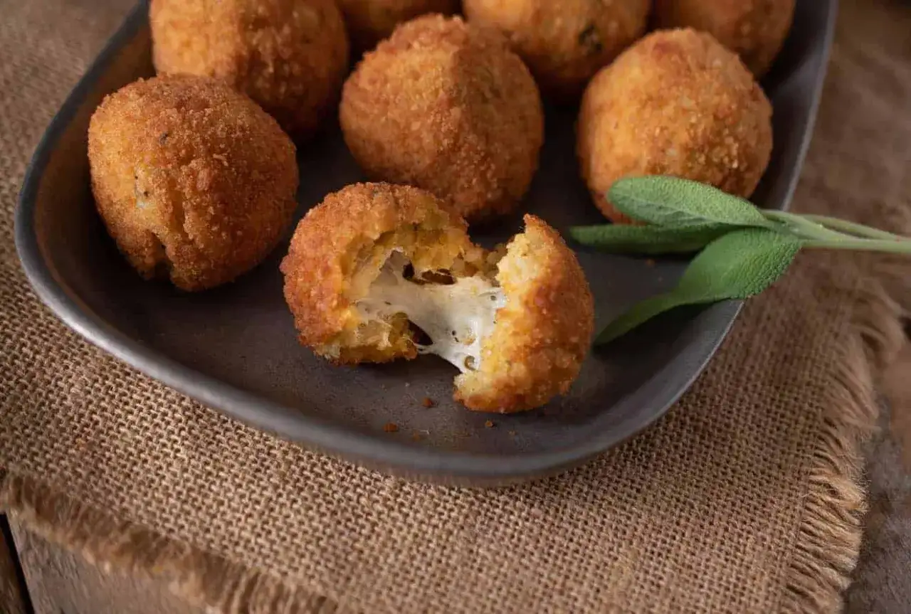 Goldbraune Arancini mit geschmolzenem K&auml;se, perfekt f&uuml;r ein italienisches arancini rezept. Frisch frittiert und mit Salbei garniert.