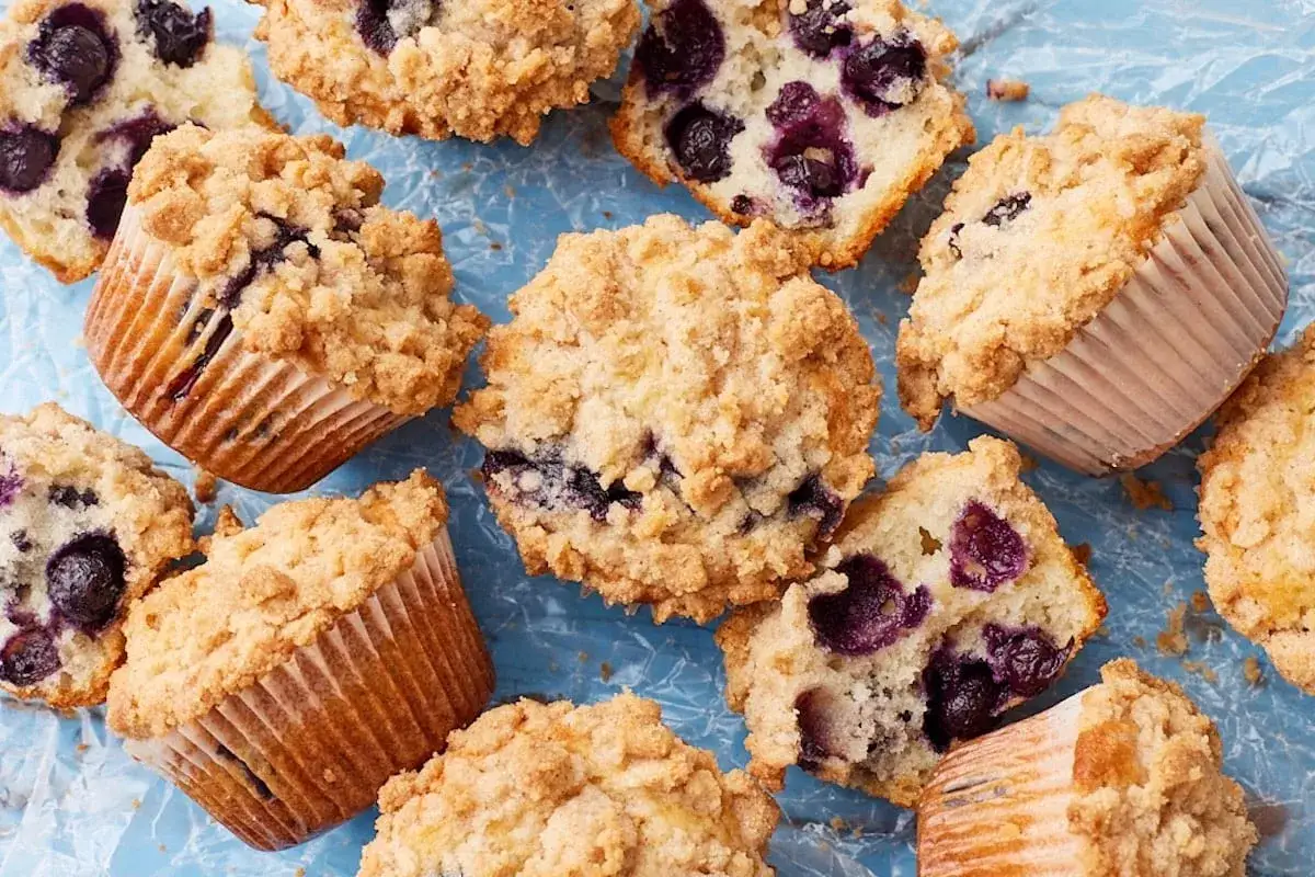 Saftige Muffins mit Blaubeeren und Streuseln, die auf einem blauen Untergrund liegen. Ein Genuss für Augen und Gaumen!
