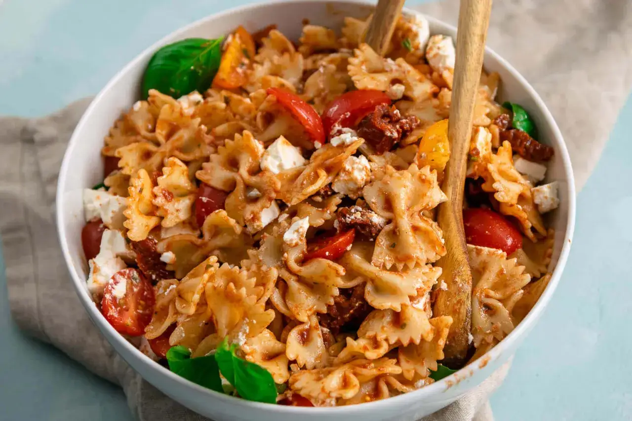 Ein k&ouml;stlicher Nudelsalat mit Farfalle, frischen Tomaten, Feta und aromatischen getrockneten Tomaten, garniert mit Basilikum.