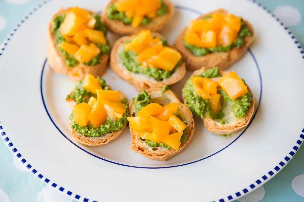 Kleine ger&ouml;stete Brotscheiben mit leuchtend gr&uuml;nem Rucola Pesto und w&uuml;rfeligen, gelben Paprikast&uuml;cken darauf.