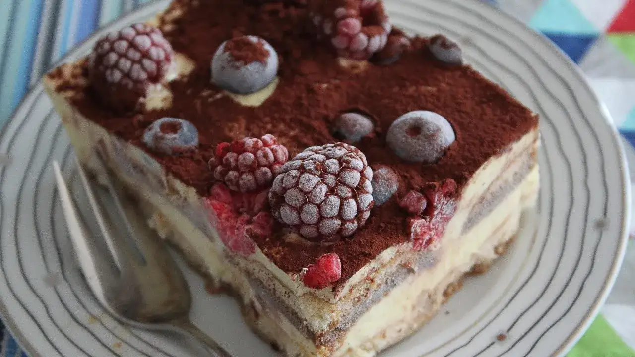 Ein St&uuml;ck Tiramisu mit gefrorenen Beeren und Kakaopulver, bereit zum Kuchen auftauen.