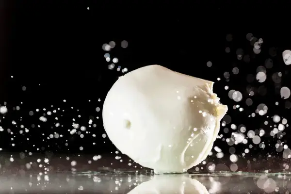 Ein frischer Fior di Latte, der auf einer spiegelnden Oberfläche liegt, umgeben von Wassertropfen und Bokeh-Lichtern.