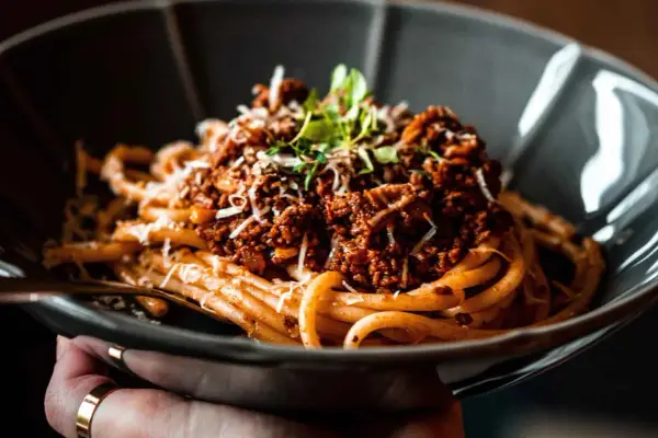 Eine Schüssel mit herzhaftem Pasta al Ragu, garniert mit frischen Kräutern und geriebenem Käse.