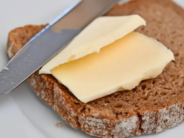 Ein Messer verteilt cremige Butter oder Margarine auf einer Scheibe dunklem Brot.