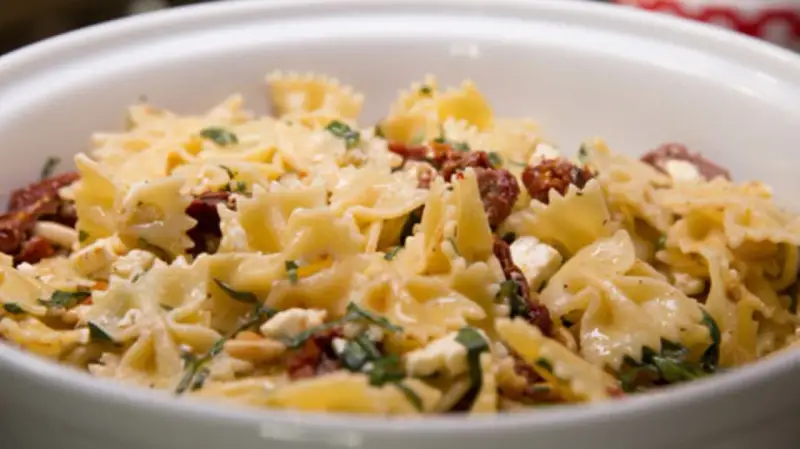 Farfalle-Nudelsalat mit getrockneten Tomaten, Feta und Pinienkernen, garniert mit frischen Kräutern. Ein köstliches Gericht.