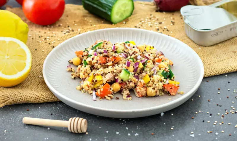 Bunter Quinoa Salat mit Kichererbsen, Tomaten, Gurken und Zwiebeln, garniert mit Zitronenspalten.